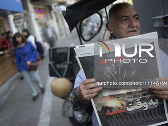 An Iranian man is sitting on a sidewalk in downtown Tehran, Iran, on April 14, 2024, holding a Jam-e Jam daily newspaper that features an il...