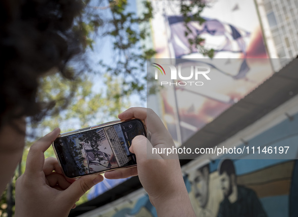 A young Iranian man is taking a photograph of an anti-Israeli mural, which celebrates the IRGC missile and UAV attack on Israel, in downtown...