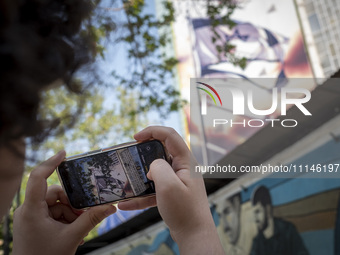 A young Iranian man is taking a photograph of an anti-Israeli mural, which celebrates the IRGC missile and UAV attack on Israel, in downtown...