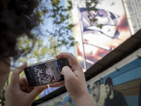 A young Iranian man is taking a photograph of an anti-Israeli mural, which celebrates the IRGC missile and UAV attack on Israel, in downtown...