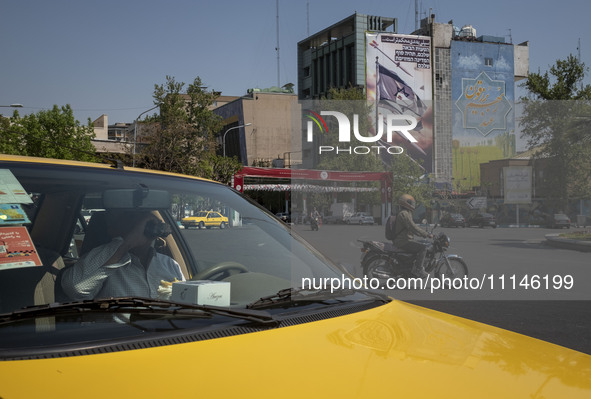 An Iranian yellow cab driver is drinking a soft drink while sitting in his cab, parked near an anti-Israeli mural in downtown Tehran, Iran,...