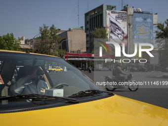 An Iranian yellow cab driver is drinking a soft drink while sitting in his cab, parked near an anti-Israeli mural in downtown Tehran, Iran,...