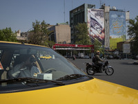 An Iranian yellow cab driver is drinking a soft drink while sitting in his cab, parked near an anti-Israeli mural in downtown Tehran, Iran,...