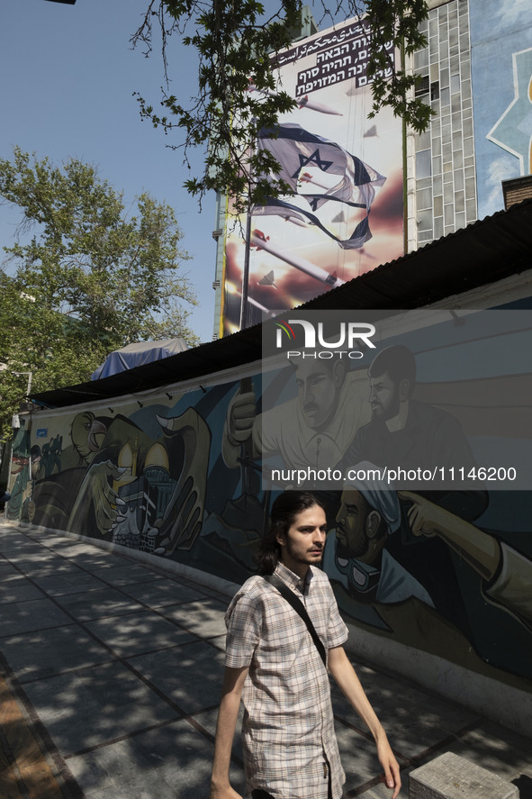 A young Iranian man is walking under an anti-Israeli mural, which celebrates the IRGC missile and UAV attack on Israel, in downtown Tehran,...