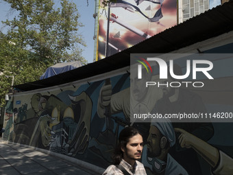 A young Iranian man is walking under an anti-Israeli mural, which celebrates the IRGC missile and UAV attack on Israel, in downtown Tehran,...