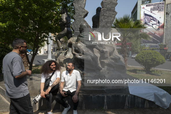 Young Iranian men are sitting and talking near an anti-Israeli mural that appreciates the IRGC missile and UAV attack on Israel, in downtown...