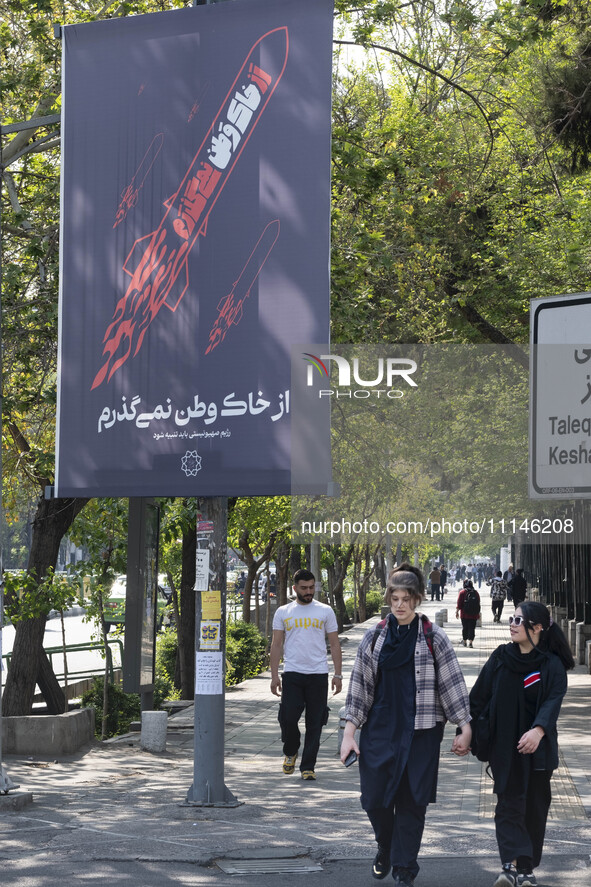 Two young Iranian women, who are not wearing mandatory headscarves, are walking past a billboard with Persian script that reads, ''I will no...