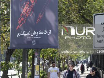 Two young Iranian women, who are not wearing mandatory headscarves, are walking past a billboard with Persian script that reads, ''I will no...