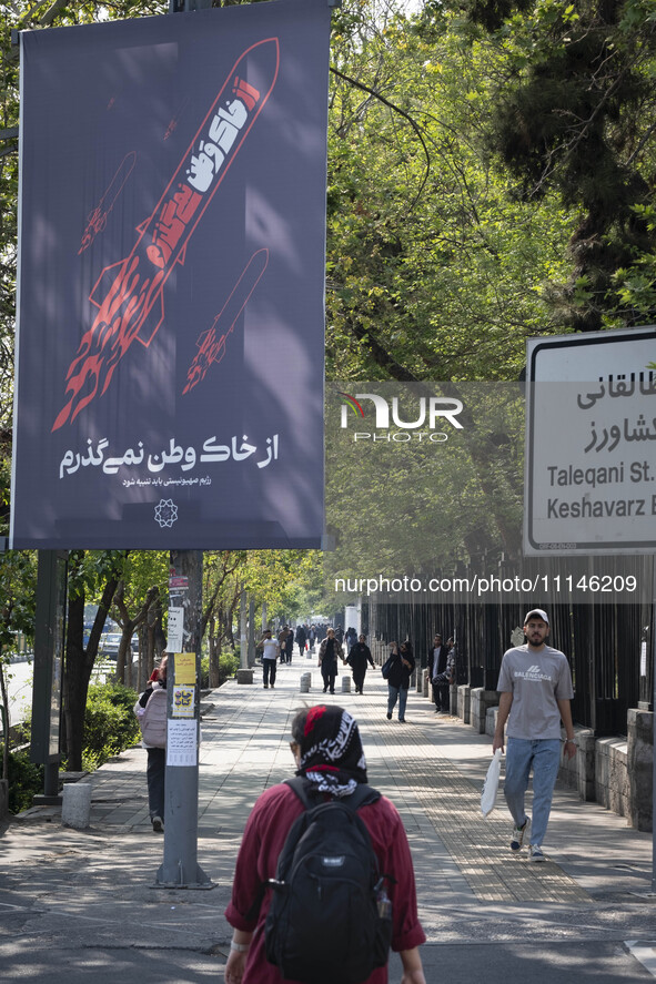 A young Iranian woman is walking past a billboard with Persian script that reads, ''I will not leave my homeland,'' which is illustrated to...