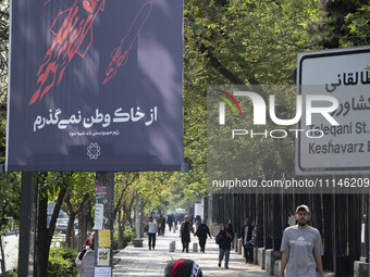 A young Iranian woman is walking past a billboard with Persian script that reads, ''I will not leave my homeland,'' which is illustrated to...