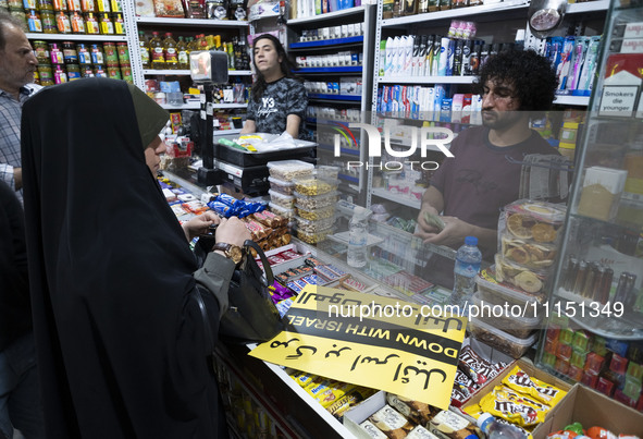 An Iranian woman, her face veiled, is shopping at a supermarket and standing next to an anti-Israeli placard as she participates in a celebr...