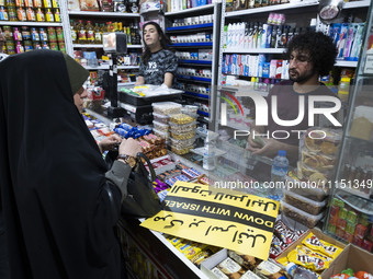 An Iranian woman, her face veiled, is shopping at a supermarket and standing next to an anti-Israeli placard as she participates in a celebr...