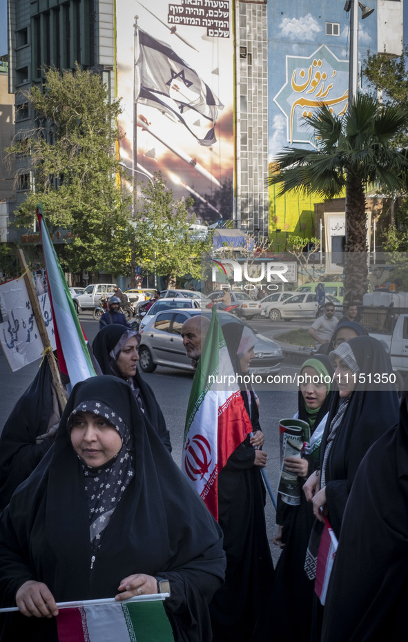 Veiled Iranian women are standing under an anti-Israeli mural, carrying Iranian flags during a gathering to celebrate the IRGC UAV and missi...