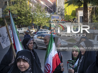 Veiled Iranian women are standing under an anti-Israeli mural, carrying Iranian flags during a gathering to celebrate the IRGC UAV and missi...