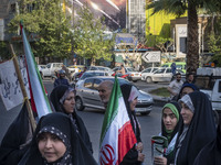 Veiled Iranian women are standing under an anti-Israeli mural, carrying Iranian flags during a gathering to celebrate the IRGC UAV and missi...