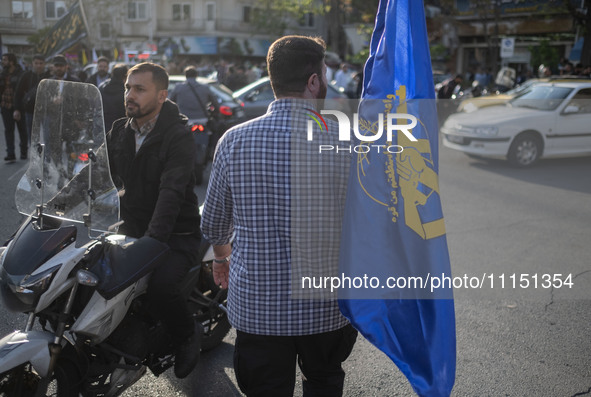 An Iranian man is carrying a flag of the Islamic Revolutionary Guard Corps during a gathering to celebrate the IRGC UAV and missile attack a...