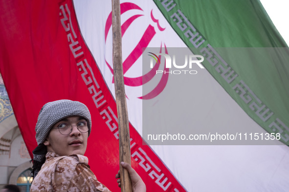 An Islamic Revolutionary Guard Corps military personnel is holding a massive Iranian flag during a gathering to celebrate the IRGC UAV and m...