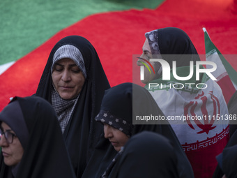 A veiled woman is standing next to a massive Palestinian flag while wearing an Iranian flag during a gathering to celebrate the IRGC UAV and...