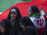 A veiled woman is standing next to a massive Palestinian flag while wearing an Iranian flag during a gathering to celebrate the IRGC UAV and...