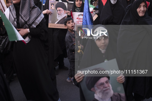 A young boy is looking on as veiled women hold portraits of Iran's Supreme Leader, Ayatollah Ali Khamenei, during a gathering to celebrate t...