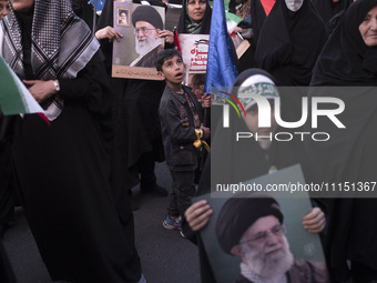 A young boy is looking on as veiled women hold portraits of Iran's Supreme Leader, Ayatollah Ali Khamenei, during a gathering to celebrate t...