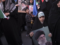 A young boy is looking on as veiled women hold portraits of Iran's Supreme Leader, Ayatollah Ali Khamenei, during a gathering to celebrate t...