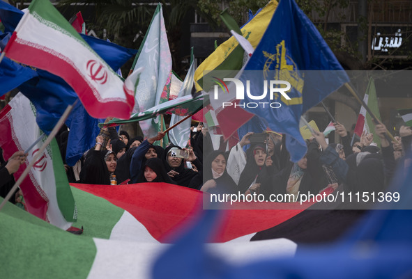 Veiled Iranian women are waving Iranian flags and those of the Islamic Revolutionary Guard Corps while standing behind a large Palestinian f...