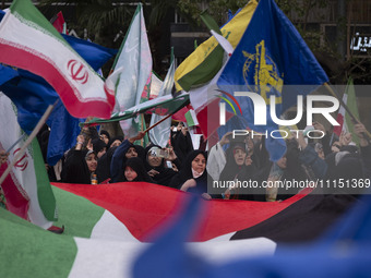 Veiled Iranian women are waving Iranian flags and those of the Islamic Revolutionary Guard Corps while standing behind a large Palestinian f...