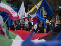 Veiled Iranian women are waving Iranian flags and those of the Islamic Revolutionary Guard Corps while standing behind a large Palestinian f...