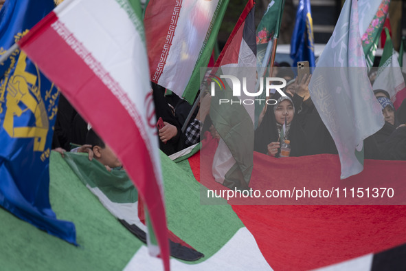 Veiled Iranian women are waving Iranian flags and those of the Islamic Revolutionary Guard Corps while standing behind a large Palestinian f...