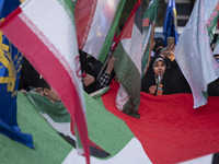 Veiled Iranian women are waving Iranian flags and those of the Islamic Revolutionary Guard Corps while standing behind a large Palestinian f...