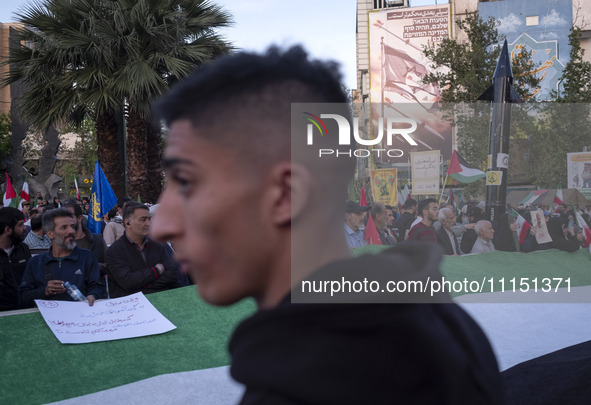 A model of Iran's first-ever hypersonic missile, Fattah (R), is being displayed next to an anti-Israeli mural while men stand behind a huge...