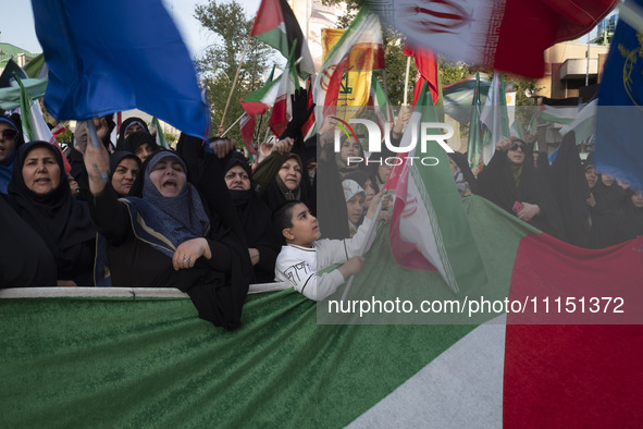 Veiled Iranian women and a young boy are waving Iranian flags while standing behind a huge Palestinian flag during a gathering to celebrate...