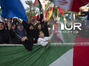 Veiled Iranian women and a young boy are waving Iranian flags while standing behind a huge Palestinian flag during a gathering to celebrate...