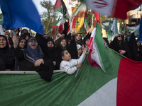 Veiled Iranian women and a young boy are waving Iranian flags while standing behind a huge Palestinian flag during a gathering to celebrate...