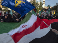 Veiled Iranian women are waving Iranian flags and those of the Islamic Revolutionary Guard Corps while standing behind a large Palestinian f...