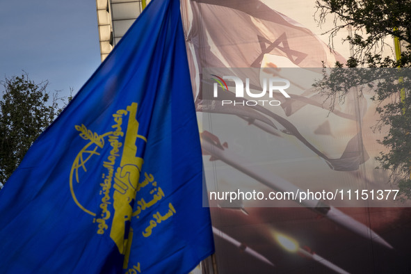 An Iranian man is waving a flag of the Islamic Revolutionary Guard Corps next to an anti-Israeli mural while celebrating the IRGC UAV and mi...