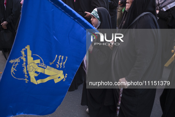 A young veiled Iranian girl is standing next to a flag of the Islamic Revolutionary Guard Corps, celebrating the IRGC UAV and missile attack...