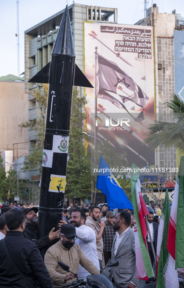 Unidentified men are holding a model of Iran's first-ever hypersonic missile, Fattah, next to an anti-Israeli mural during a gathering to ce...