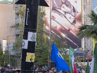 Unidentified men are holding a model of Iran's first-ever hypersonic missile, Fattah, next to an anti-Israeli mural during a gathering to ce...