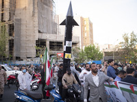 Two unidentified men are carrying a model of Iran's first-ever hypersonic missile, Fattah, by a motorcycle during a gathering to celebrate t...