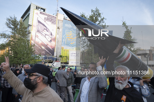 Unidentified men are carrying a model of Iran's first-ever hypersonic missile, Fattah, past an anti-Israeli mural during a gathering to cele...