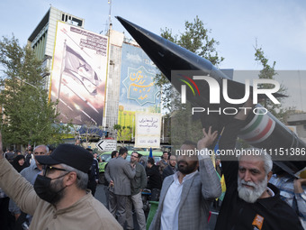 Unidentified men are carrying a model of Iran's first-ever hypersonic missile, Fattah, past an anti-Israeli mural during a gathering to cele...