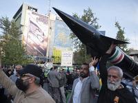 Unidentified men are carrying a model of Iran's first-ever hypersonic missile, Fattah, past an anti-Israeli mural during a gathering to cele...