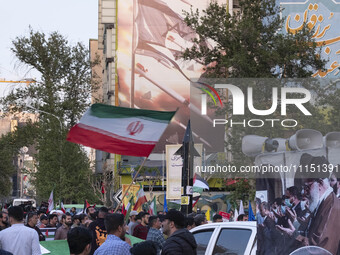 A man is waving an Iranian flag next to a model of Iran's first-ever hypersonic missile, Fattah, under an anti-Israeli mural during a gather...