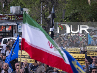 A man is waving an Iranian flag in front of a model of Iran's first-ever hypersonic missile, Fattah, during a gathering to celebrate the IRG...