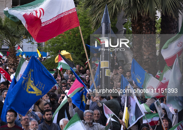 Men are waving Iranian flags and flags of the Islamic Revolutionary Guard Corps while a model of Iran's first-ever hypersonic missile, Fatta...