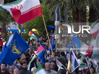 Men are waving Iranian flags and flags of the Islamic Revolutionary Guard Corps while a model of Iran's first-ever hypersonic missile, Fatta...