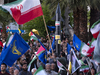 Men are waving Iranian flags and flags of the Islamic Revolutionary Guard Corps while a model of Iran's first-ever hypersonic missile, Fatta...