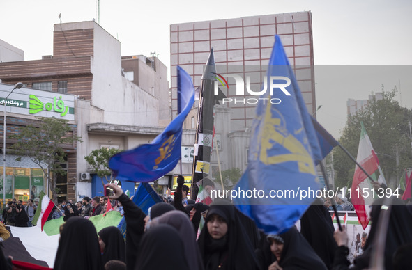 Veiled women are waving Iranian flags and flags of the Islamic Revolutionary Guard Corps while a model of Iran's first-ever hypersonic missi...